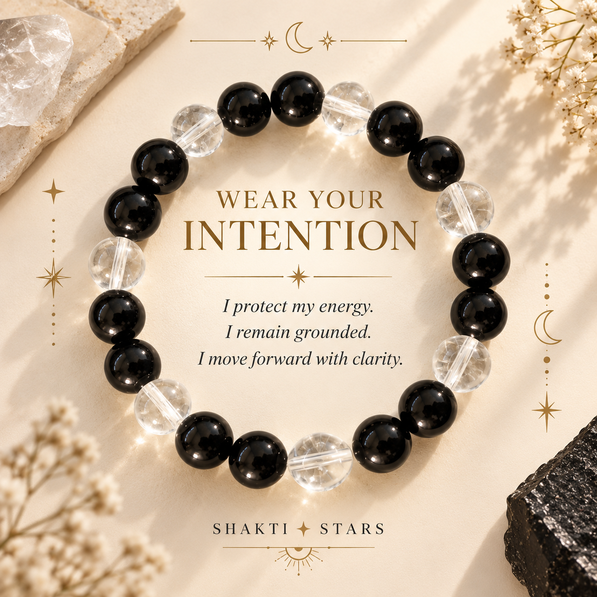 A beaded bracelet arranged in a circle on a warm beige surface, featuring alternating glossy black beads and clear faceted crystal beads. Decorative dried flowers, crystals, and gold-toned stars frame the image, with the text 'WEAR YOUR INTENTION' and a quote in the center.