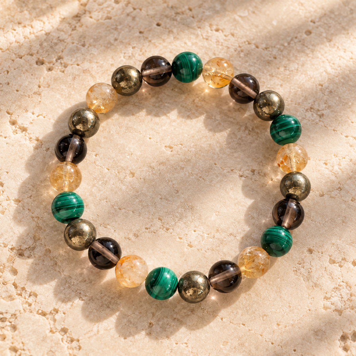A beaded stretch bracelet made of polished gemstone-like beads in green, black, smoky brown, and translucent amber, arranged in a circle on a light beige textured stone surface.