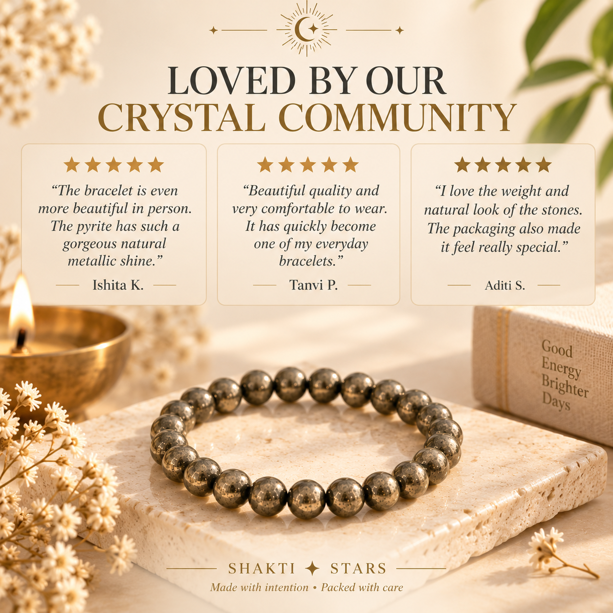 A beaded bracelet made of polished metallic marbled beads is displayed on a stone surface with dried flowers, a candle, and a book in a warm styled setting. The image includes promotional text reading 'LOVED BY OUR CRYSTAL COMMUNITY' and a brand name 'SHAKTI STARS' at the bottom.