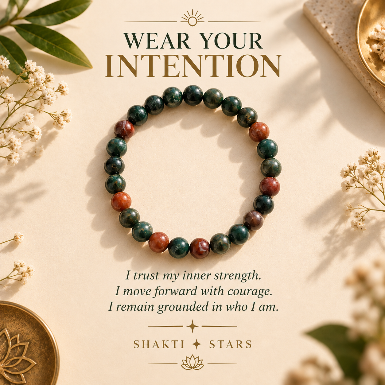 A beaded stretch bracelet made of dark green, reddish-brown, and black stone beads, displayed on a warm beige background with decorative botanicals and text that reads 'WEAR YOUR INTENTION' and 'SHAKTI STARS'.
