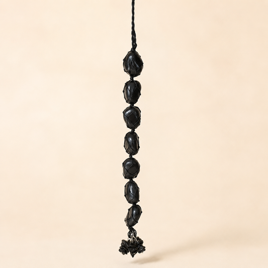 A black beaded hanging ornament with faceted round beads and a small tassel, suspended against a plain beige background.