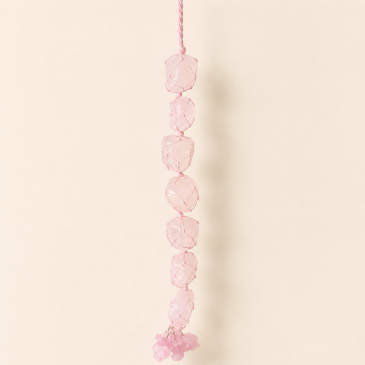 A pink beaded hanging ornament made of faceted pink stone beads strung on a pink cord, shown against a plain warm beige background.