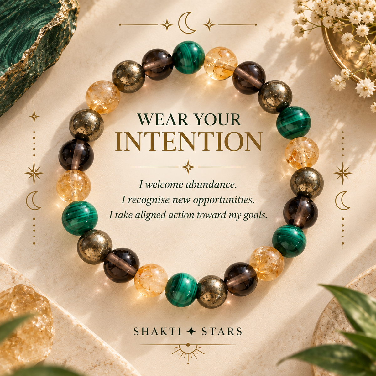 A beaded intention bracelet arranged in a circle on a warm cream surface with decorative crystals and leaves. The bracelet features translucent green, smoky brown, gold, and amber beads.