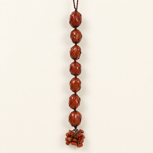 A vertical hanging beaded ornament made of glossy reddish-brown oval beads with a dark cord, photographed against a plain warm off-white background.