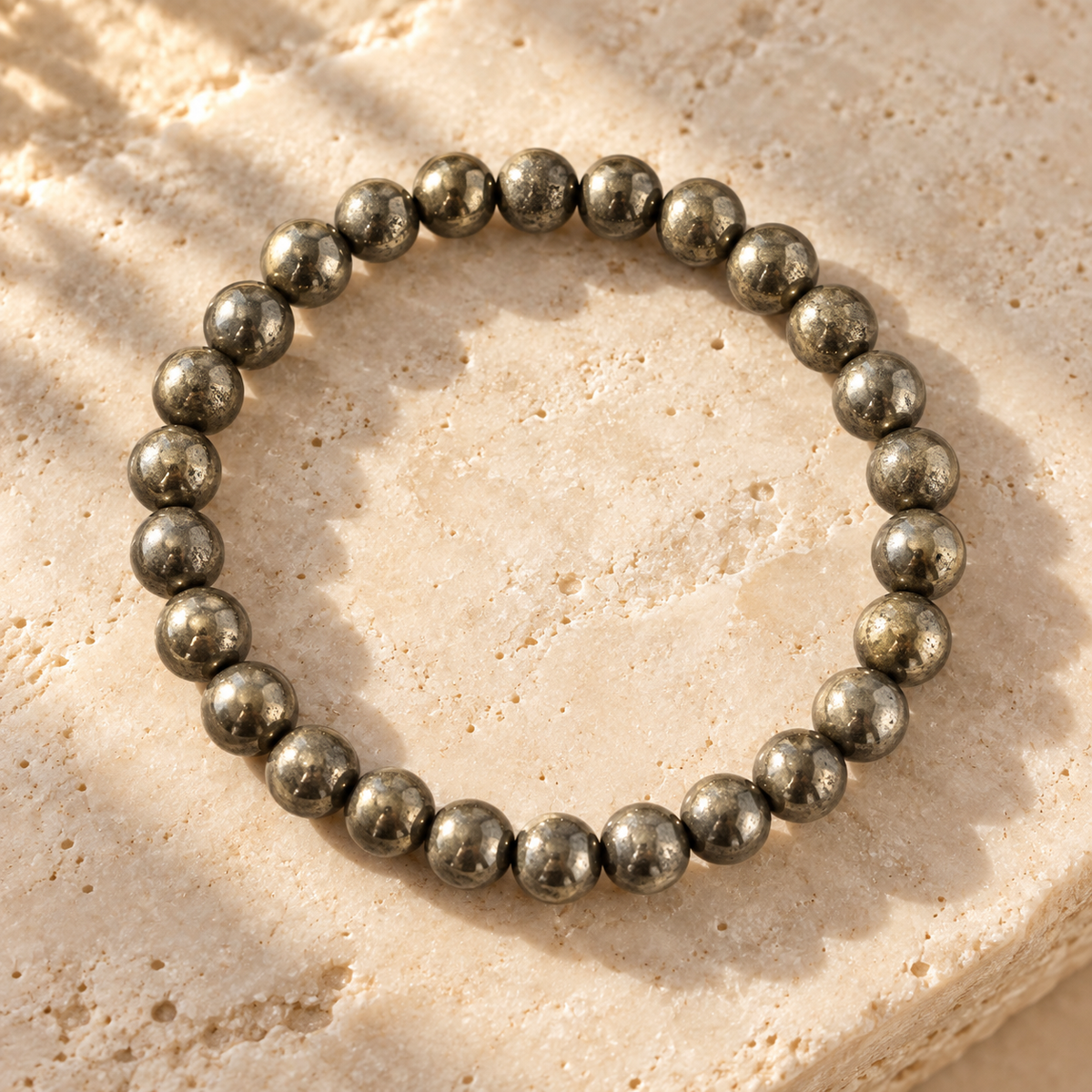 A beaded stretch bracelet made of polished metallic gray round beads, arranged in a circle on a textured beige stone surface.