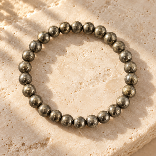 A beaded stretch bracelet made of polished metallic gray round beads, arranged in a circle on a textured beige stone surface.