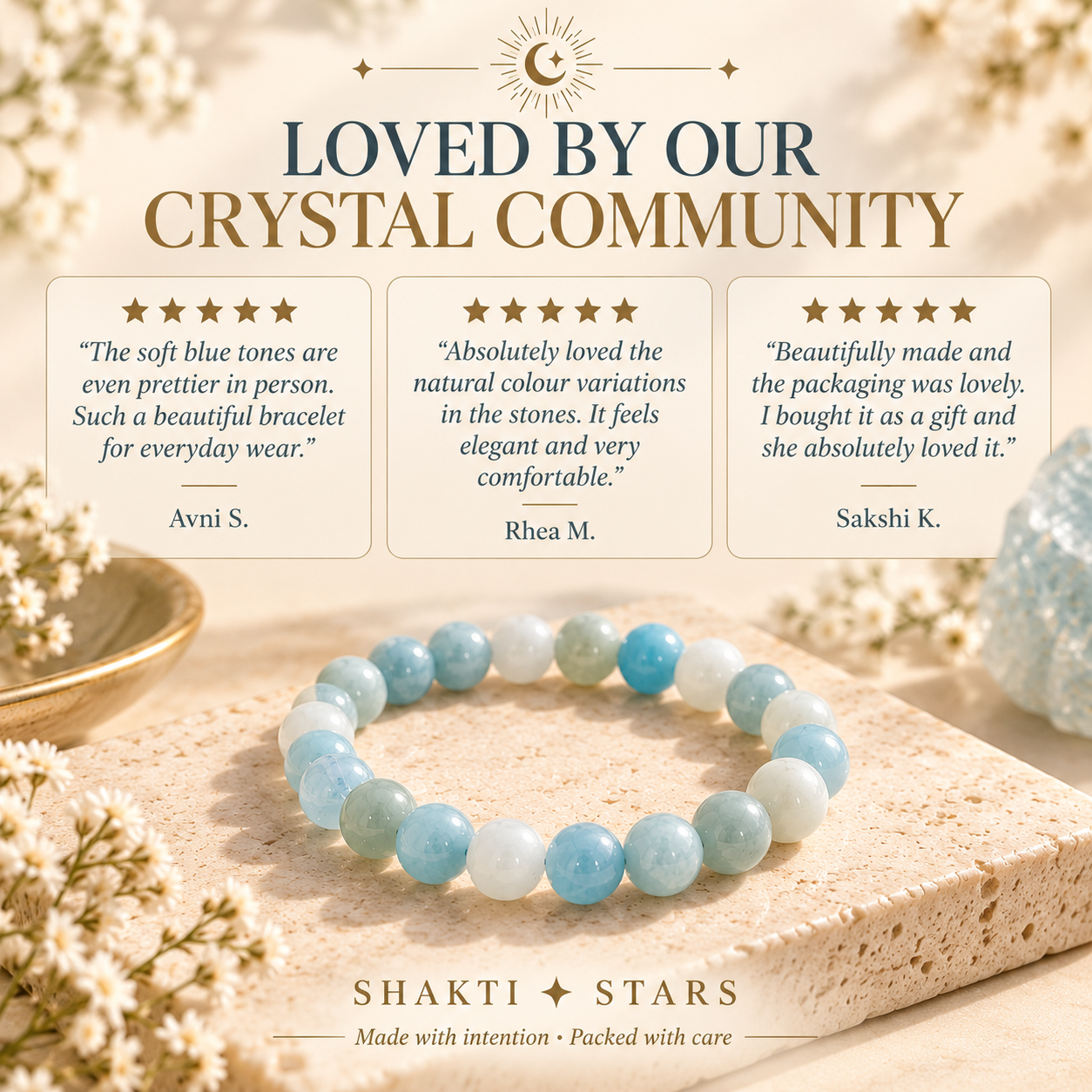A beaded bracelet made of light blue and white marbled gemstones is displayed on a textured stone surface with decorative dried flowers and a bowl in the background. The image includes promotional text reading 'LOVED BY OUR CRYSTAL COMMUNITY' with three customer reviews and the brand name 'SHAKTI STARS' at the bottom.